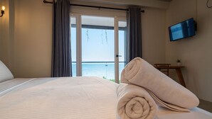 Habitación de hotel con una cama grande, un televisor en la pared y vista al mar por la ventana.