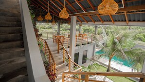 Una terraza exterior de varios niveles con barandas de madera, lámparas de mimbre colgantes y un área de piscina con una palmera.