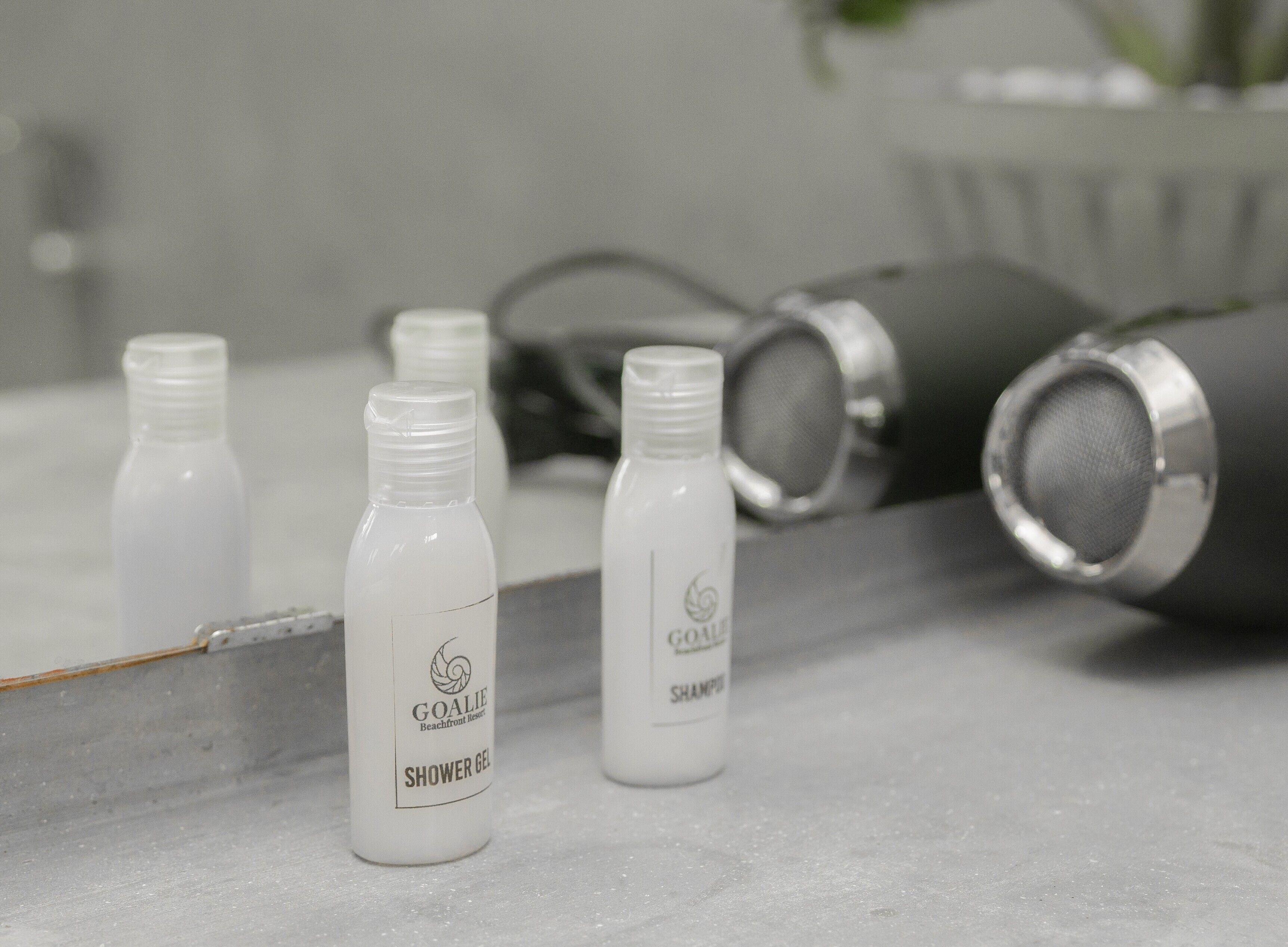 Four bottles of shower gel and a grey hairdryer on a countertop.