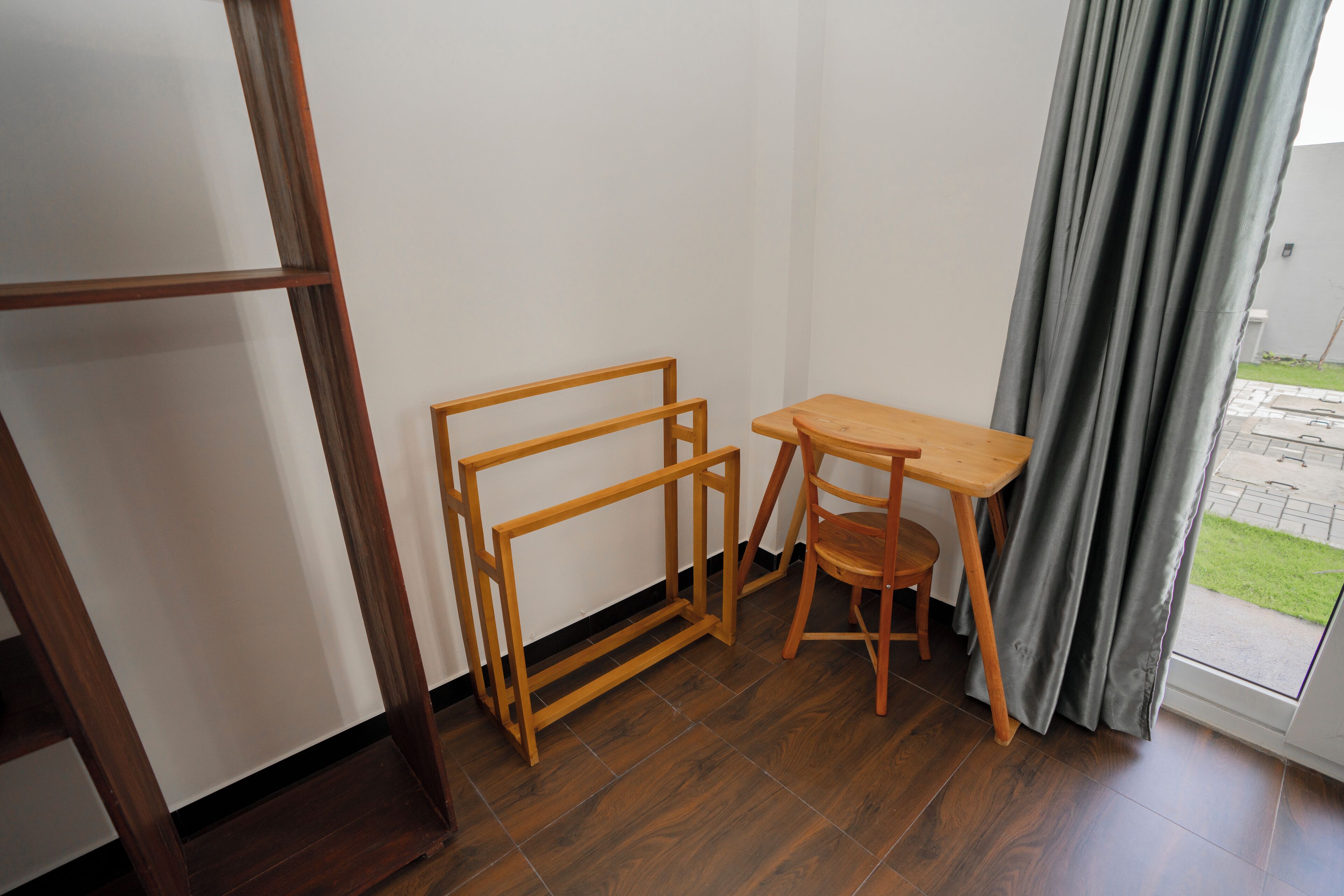 A room with a wooden floor, a small wooden table, a chair, and a metal shelf unit.