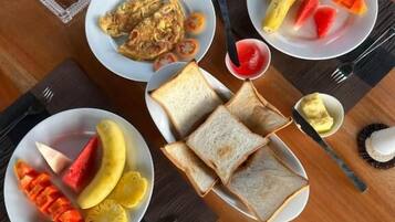 Una mesa de comedor con platos de comida, incluyendo tostadas, fruta y un recipiente pequeño con mantequilla.