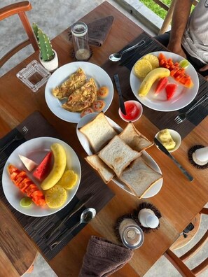 Una mesa de comedor con platos de comida, incluyendo tostadas, fruta y un recipiente pequeño con mantequilla.