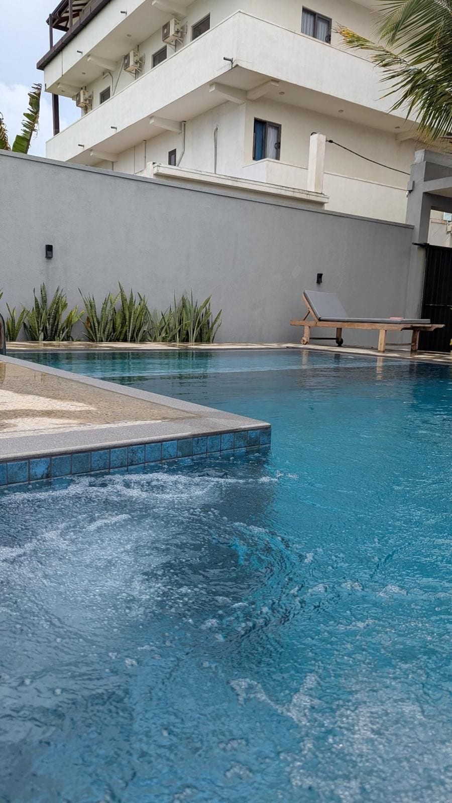 Une piscine avec un fauteuil de relaxation et un bâtiment en arrière-plan.