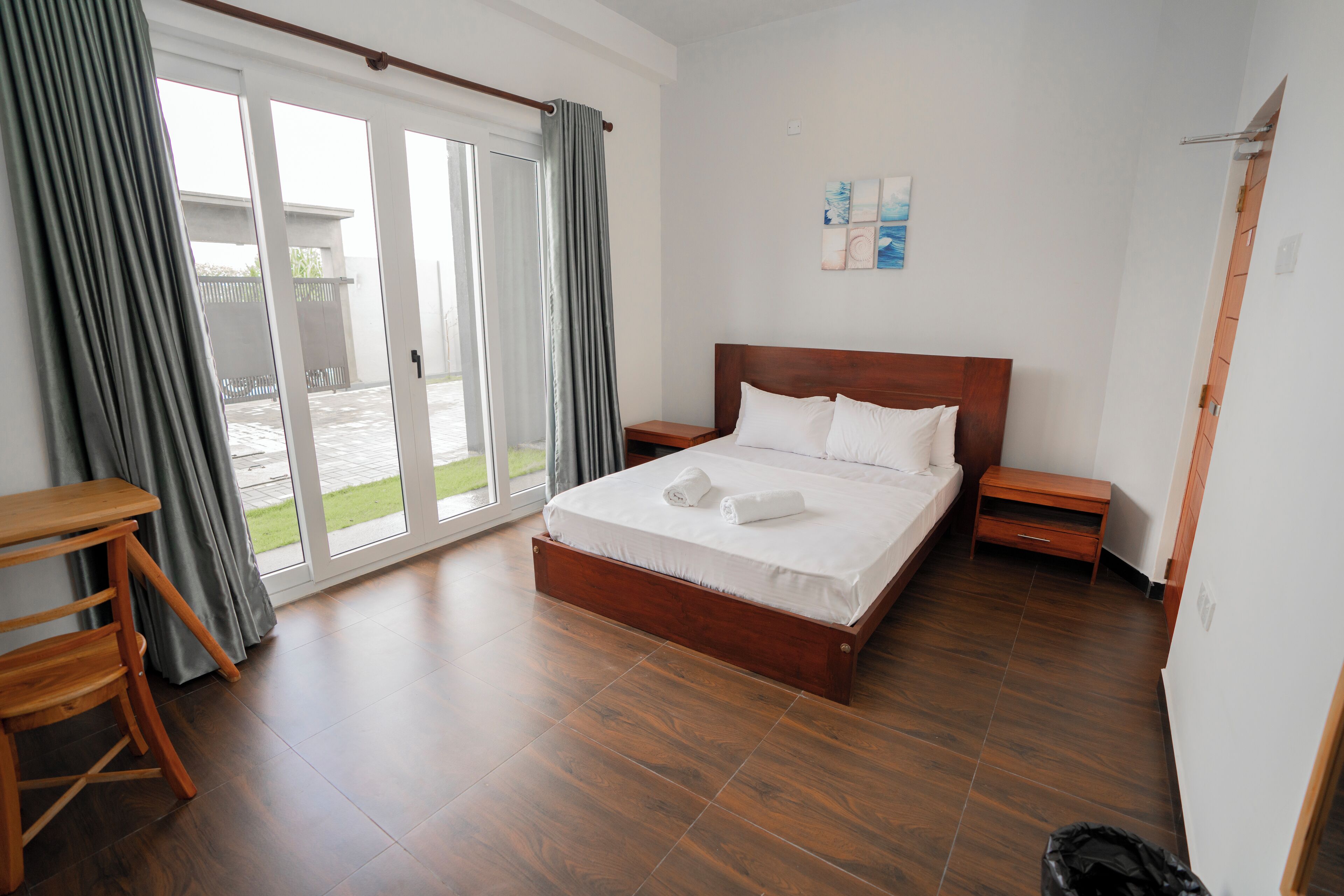 A bedroom with a wooden bed, a wooden nightstand, a small wooden table, and a sliding glass door leading to an outdoor area.