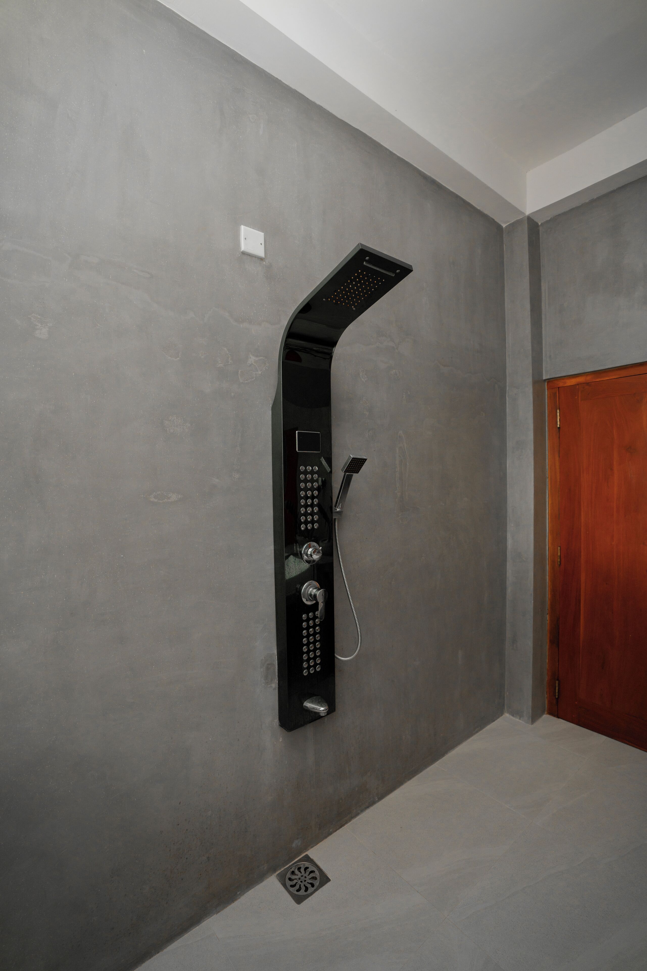 A modern shower with a control panel and a wooden door in a bathroom with grey walls.