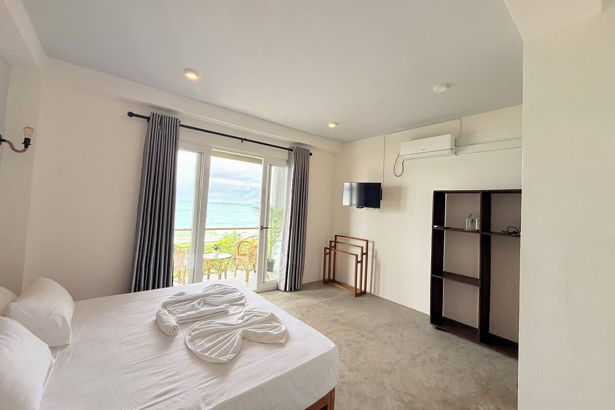 Une chambre d’hôtel équipée d’un lit, d’une télévision, d’une armoire et d’un balcon avec vue sur la mer.
