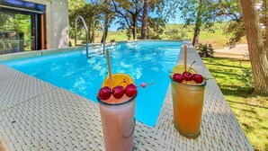Escena junto a la piscina con dos bebidas sobre una mesa de mimbre, una piscina azul cristalina y vistas a un campo de golf.
