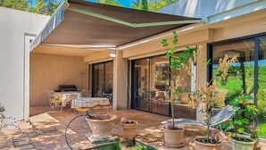Un patio exterior con zona de estar techada, plantas en macetas y vistas del paisaje circundante.