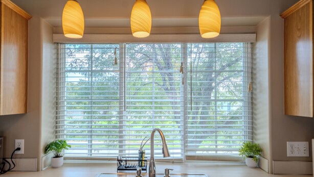 Une cuisine avec deux éviers, une fenêtre avec des stores et des luminaires suspendus.