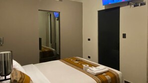 Une chambre d’hôtel avec un lit, un téléviseur fixé au mur, un miroir, une porte et un luminaire au plafond.