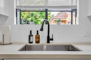 Une cuisine avec un évier en acier inoxydable, un robinet noir et deux bouteilles posées sur le comptoir.