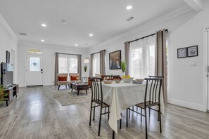 Un vaste espace dédié à la salle à manger, avec une table dressée pour quatre personnes, entourée de chaises, et une vue sur l’extérieur grâce à de grandes fenêtres.
