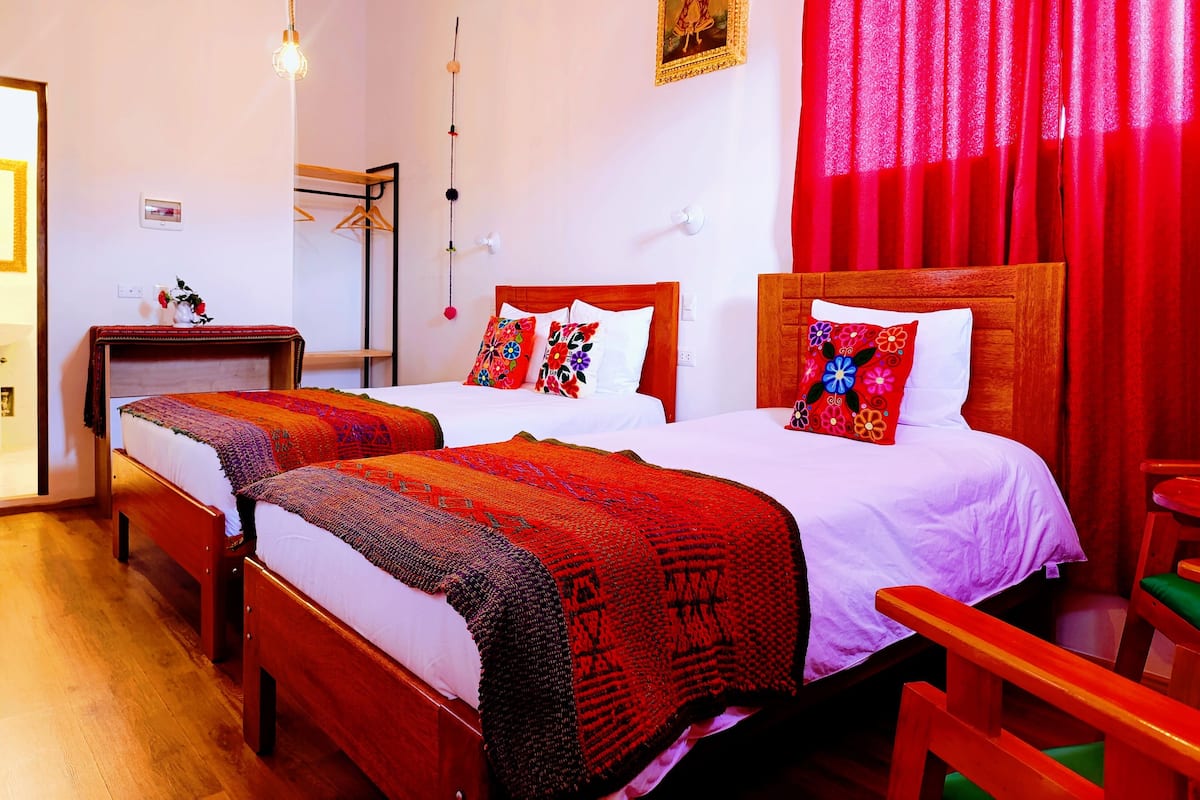 A hotel room with two wooden beds, each with a red and white bedspread, and a red curtain.