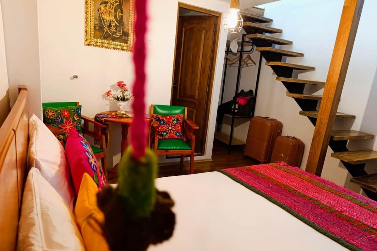 A bedroom with a bed, a chair, a table with a vase of flowers, a staircase, and a door.