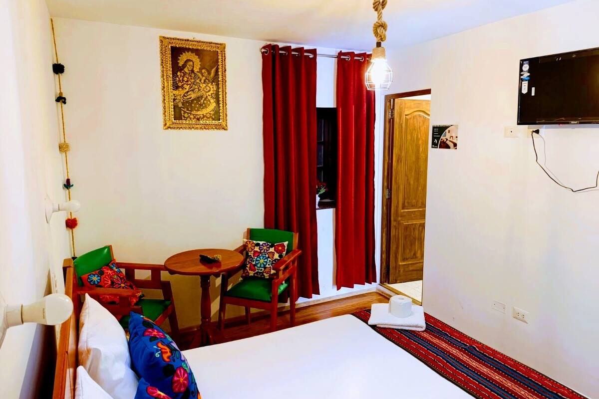 A hotel room with a bed, a small table with chairs, a wall-mounted TV, and a door.