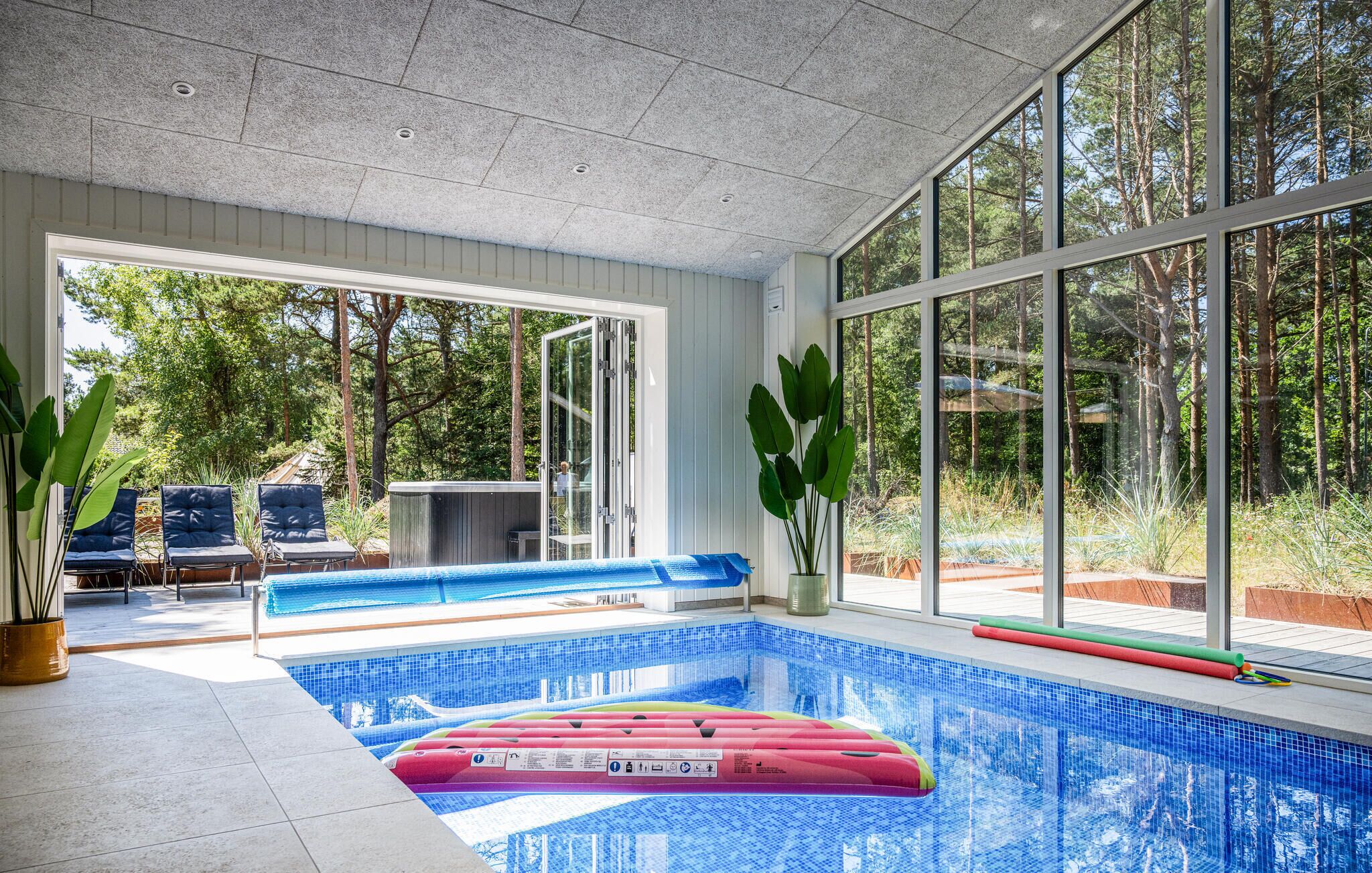 En indendørs swimmingpool med glasvægge, blå flisegulv og en bænk.