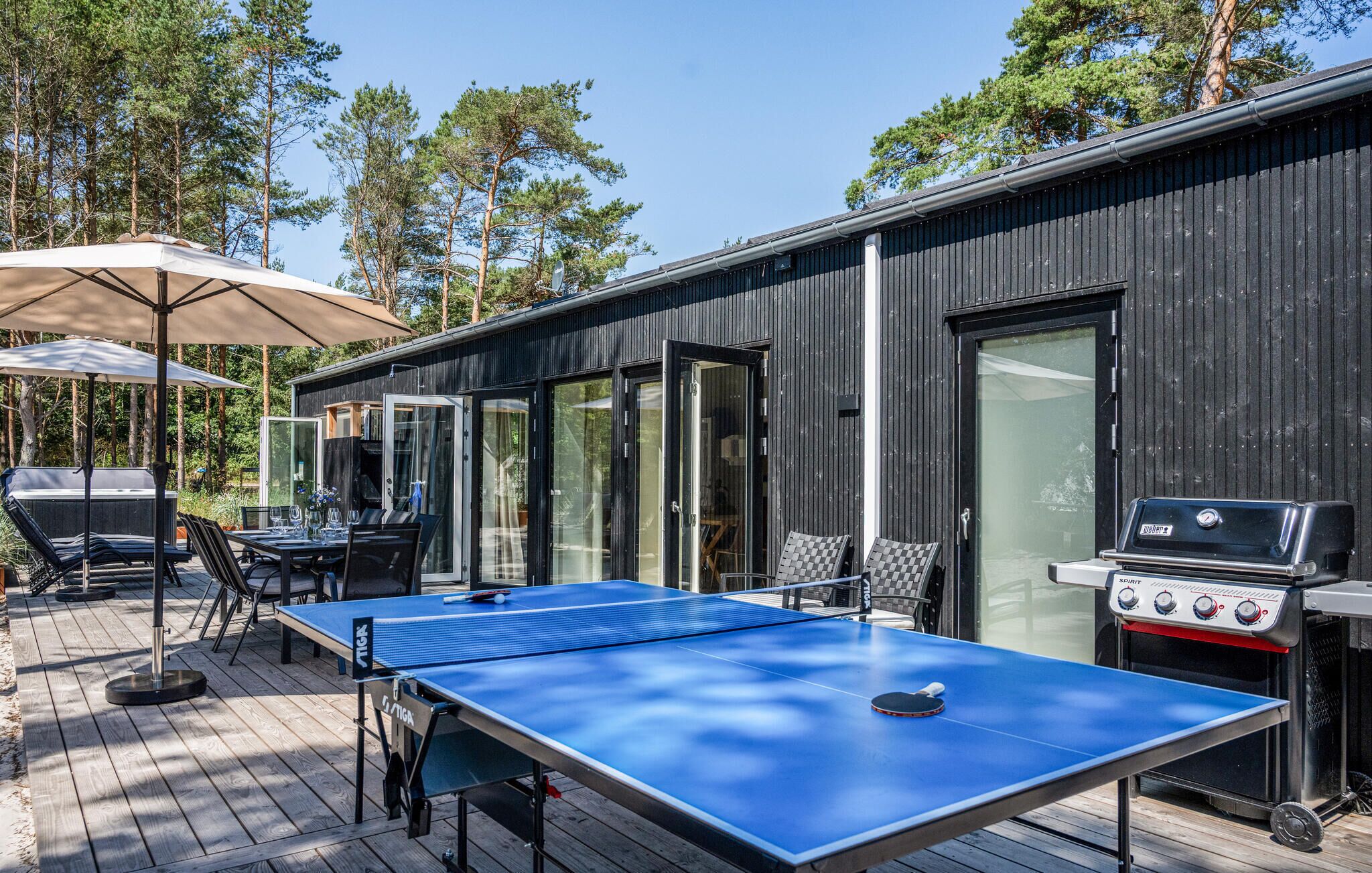 An outdoor deck with a ping pong table, chairs, a barbecue grill, and a covered seating area.