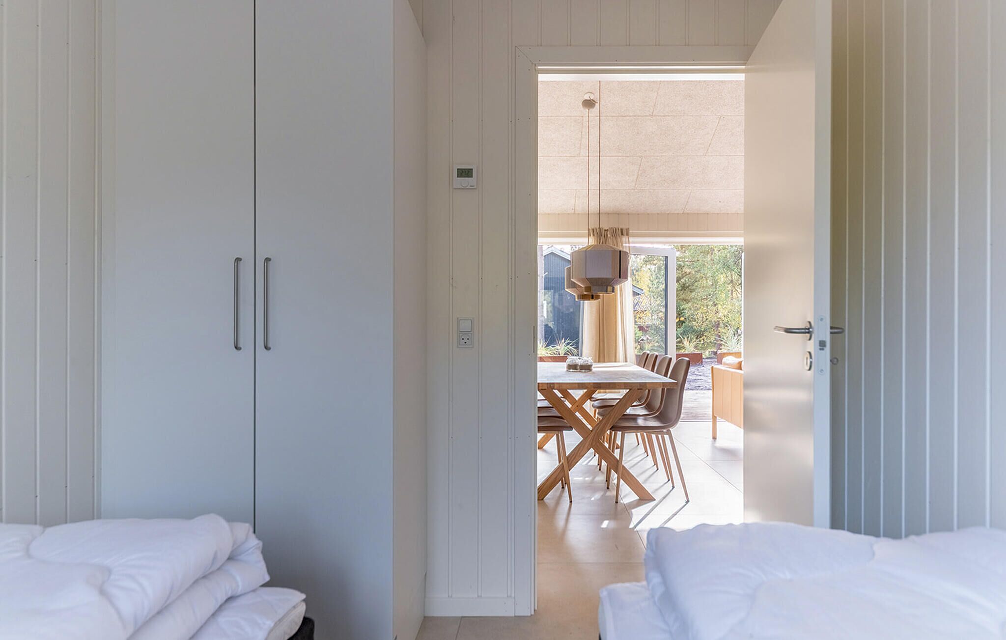 A modern hotel room with white walls, a wooden dining table, and a view of the garden.