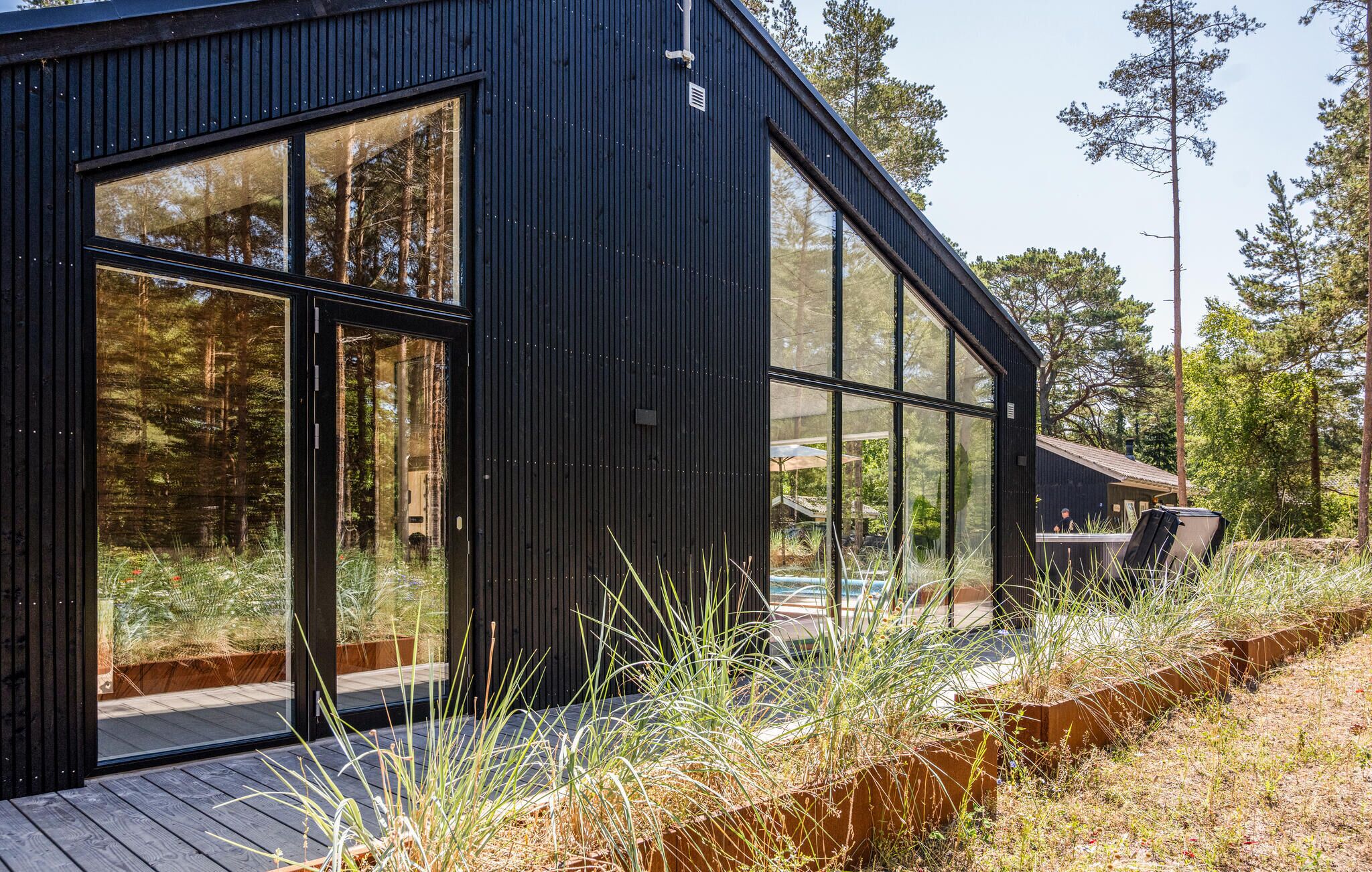 Un bâtiment moderne doté de grandes fenêtres, d’une terrasse en bois et entouré d’un cadre naturel.