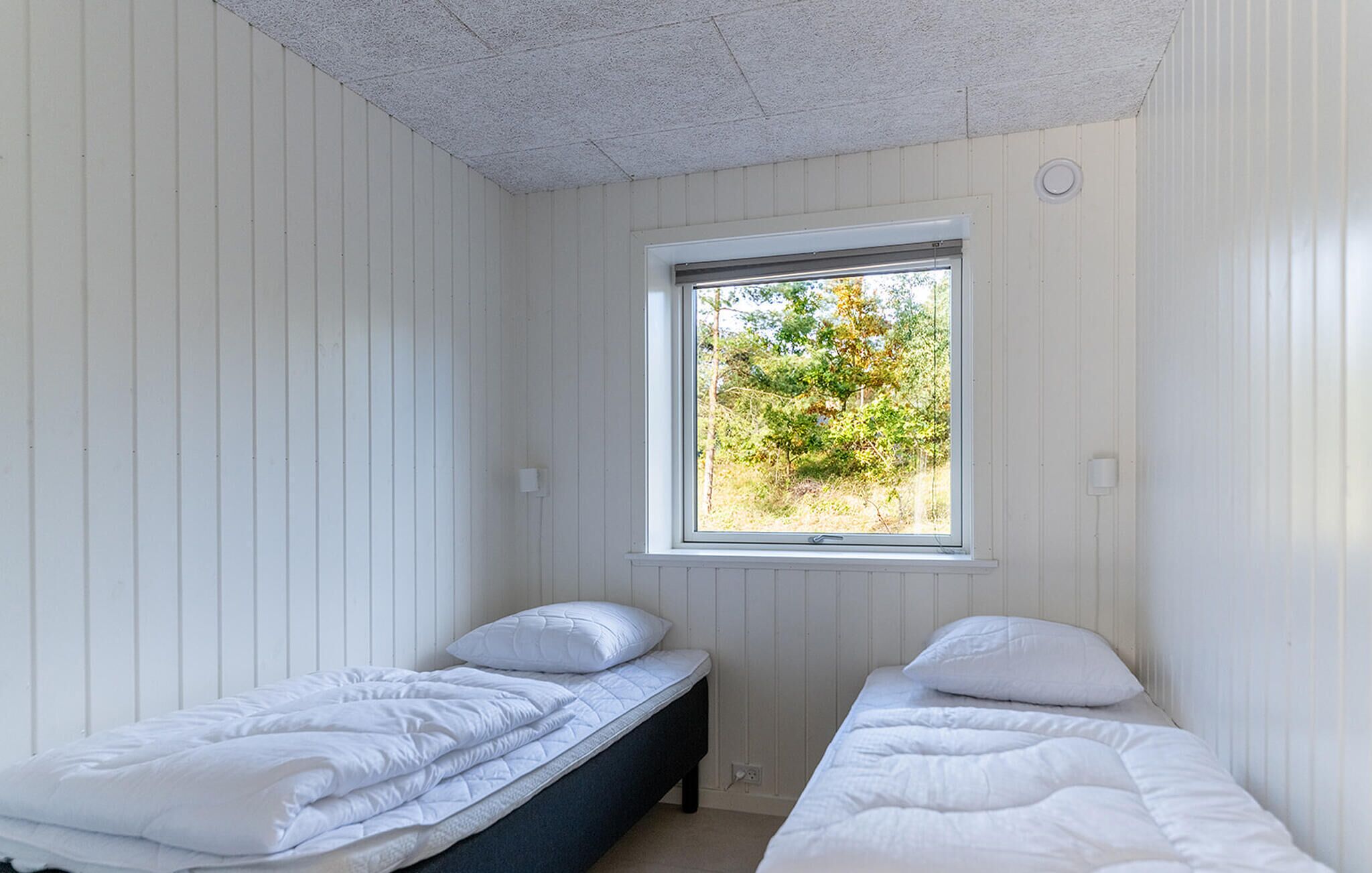 Ein kleines Schlafzimmer mit einem Bett, einem Fenster mit Blick auf Bäume und weißen Wänden.