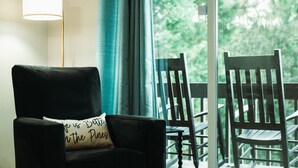 A black leather chair with a cushion that reads "Life is Better on the Pincers" and a wooden chair on a balcony with a view of trees. - Three Little Pines Condo 2BD 2BA with Pool Close to Village and Pinehurst Resort (Pinehurst)