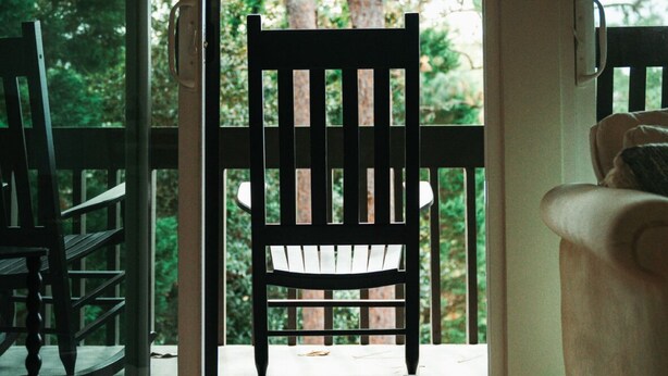 A wooden chair facing a glass door with a view of trees. - Three Little Pines Condo 2BD 2BA with Pool Close to Village and Pinehurst Resort (Pinehurst)