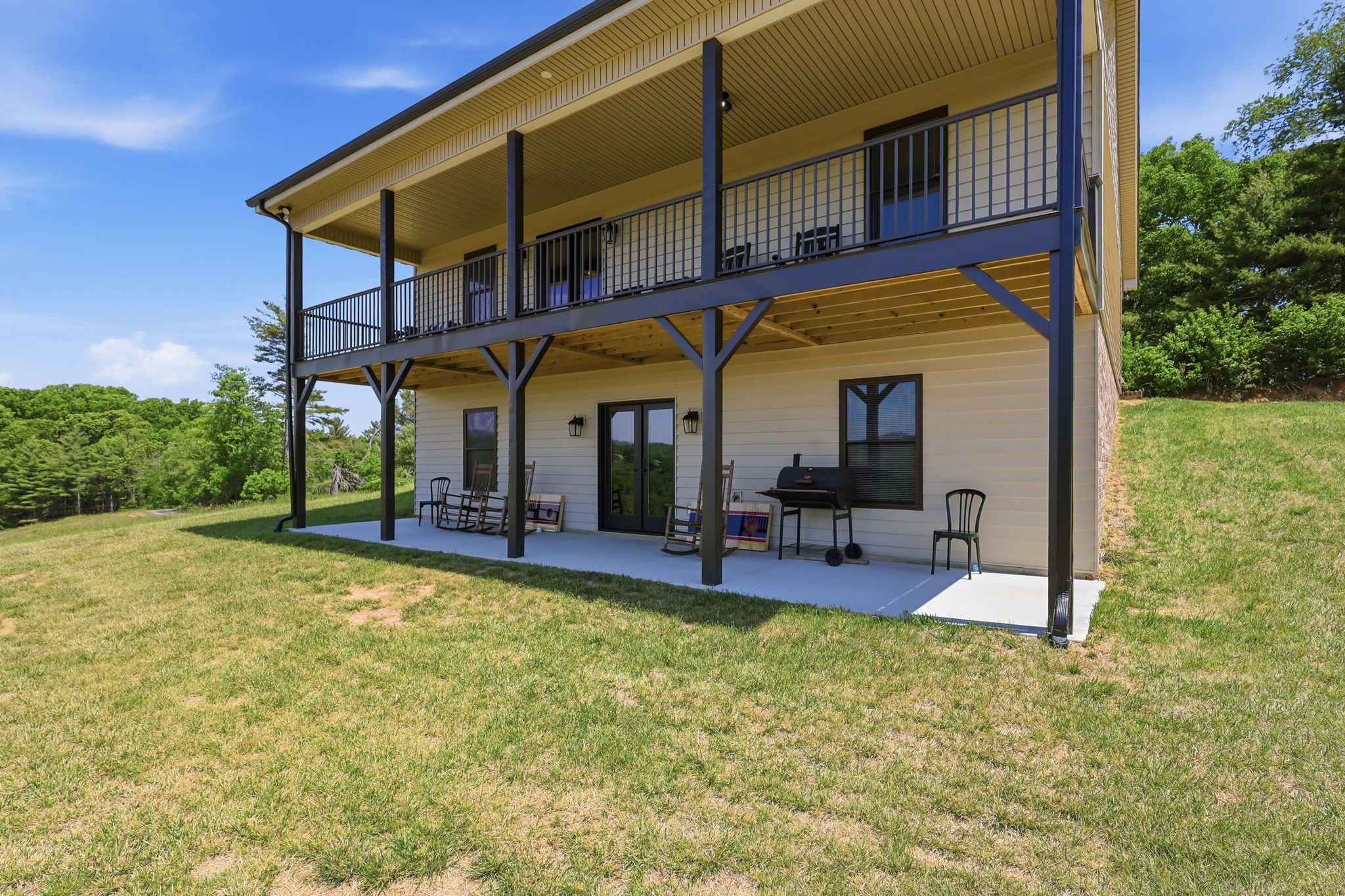 A two-story house with a balcony, a patio with chairs, and a grill.
