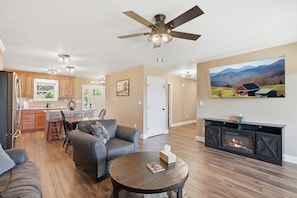 A living room with a fireplace, a ceiling fan, and a large painting of a landscape.