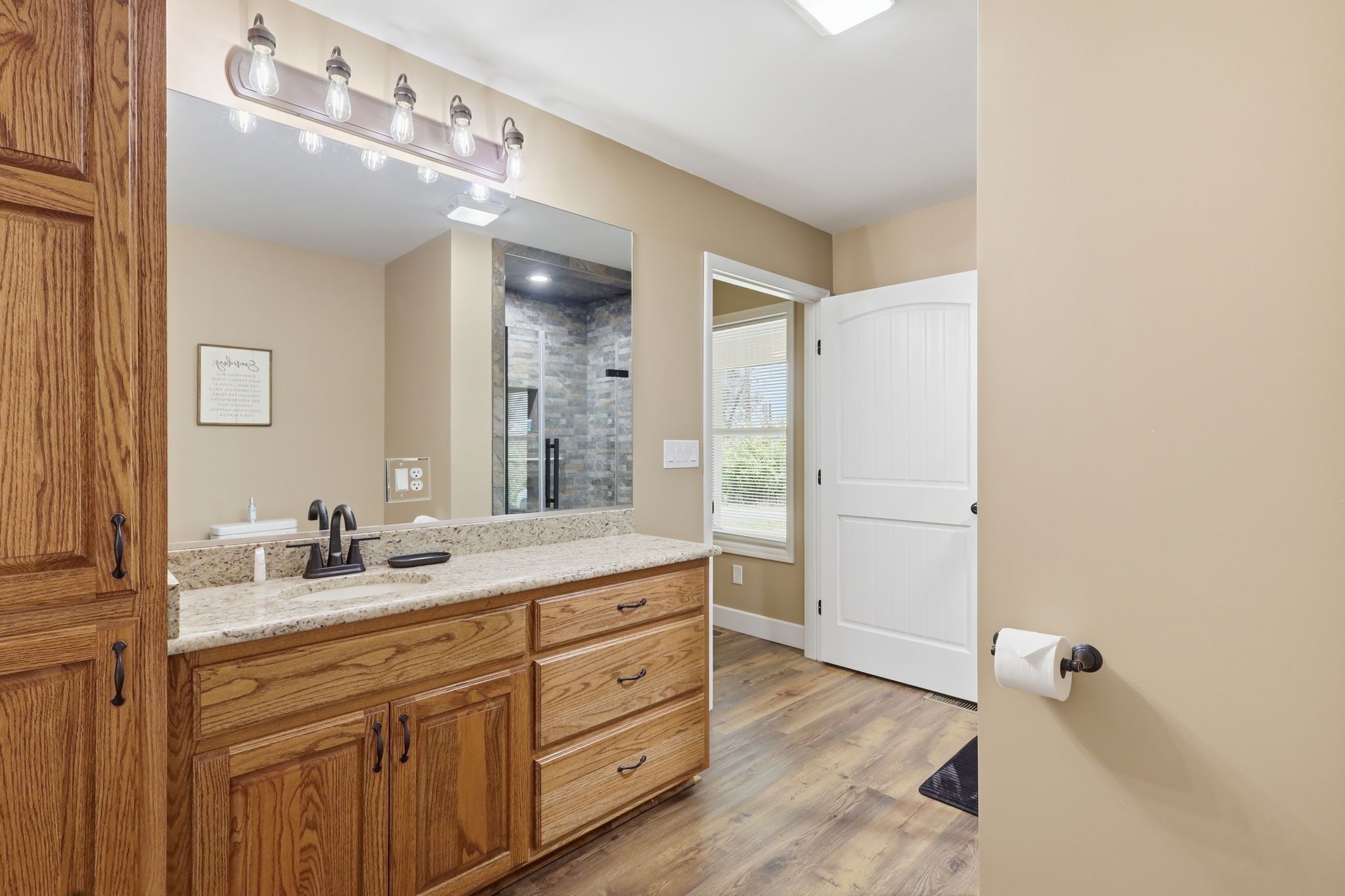 A bathroom with wooden cabinets, a granite countertop, a mirror, and a white door.