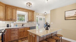 Una cocina con armarios de madera, encimera de granito, una isla integrada con taburetes e iluminación colgante.