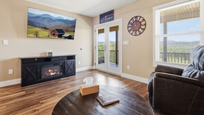 Una sala de estar con chimenea, un cuadro de paisaje grande, un cartel de bienvenida, un reloj y vistas a través de una ventana.