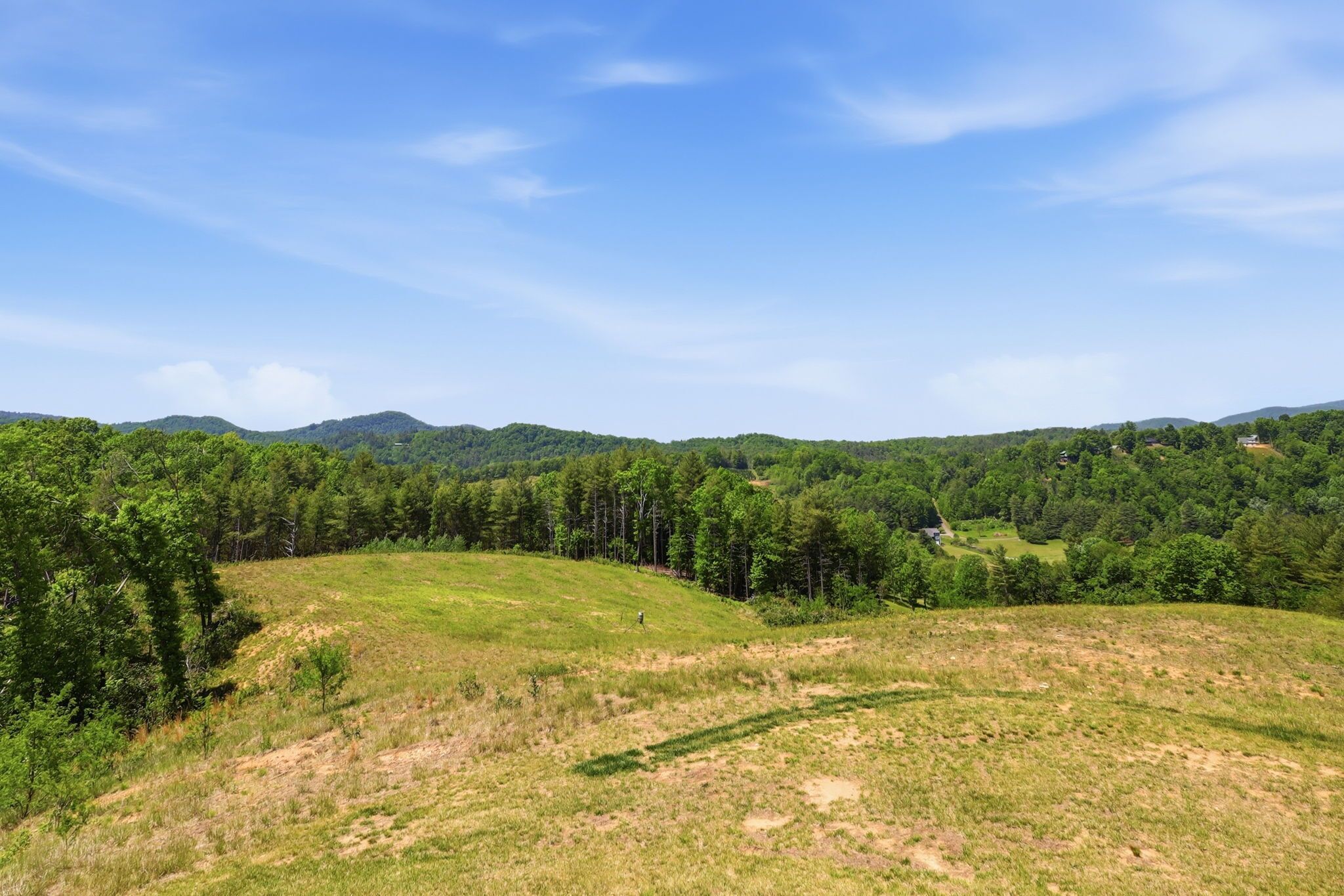 Eine hügelige Landschaft mit blauem Himmel, dichtem Wald und einem kleinen Gebäude in der Ferne.