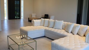 A modern living room with a large sectional sofa, a glass coffee table, and a chandelier. - New Luxury Palm Springs Home for Family & Friends (Palm Springs)