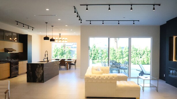 A modern kitchen with a central island, dining area with chairs, a sofa, and a large window with a view of greenery. - New Luxury Palm Springs Home for Family & Friends (Palm Springs)