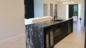 A modern kitchen with a marble island, stainless steel appliances, and pendant lighting. - New Luxury Palm Springs Home for Family & Friends (Palm Springs)