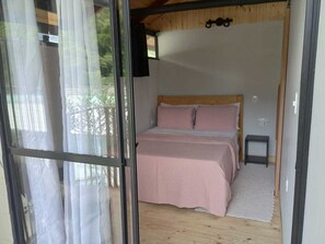 A bedroom with a wooden bed, a small bedside table, and a window with sheer curtains. - Duplex chalet recanto monte fuji ubatumirim  (Ubatuba)