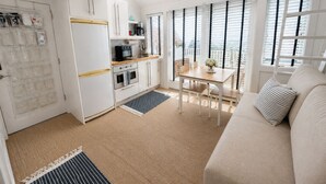 A compact kitchen with a dining area, a sofa, and a view through the window.