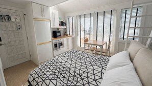 A bedroom with a geometric-patterned bedspread, a kitchenette with a refrigerator, oven, and microwave, and a dining area with a table and chairs.