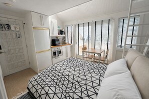 Une chambre avec une couvre-lit à motifs géométriques, une kitchenette équipée d’un réfrigérateur, d’un four et d’un four à micro-ondes, et un coin repas avec une table et des chaises.
