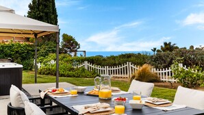 An outdoor dining area with a table set for breakfast, a hot tub, and a scenic view of the ocean.