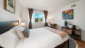 A bedroom with a bed, bedside lamps, a desk, and a window with curtains.
