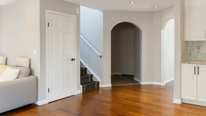 A hallway with a wooden floor, white walls, and a staircase leading to another room. - Blue-bell Cottage w/Garage, Fireplace & Backyard (Calgary)