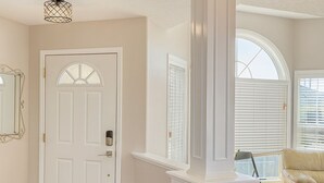 A room with a white door, a white column, a beige sofa, and a window with blinds. - Blue-bell Cottage w/Garage, Fireplace & Backyard (Calgary)