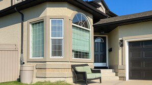 A residential house with a garage, a covered entryway, and a front porch with a chair. - Blue-bell Cottage w/Garage, Fireplace & Backyard (Calgary)