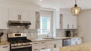 A modern kitchen with white cabinetry, a stainless steel stove, and a marble countertop. - Blue-bell Cottage w/Garage, Fireplace & Backyard (Calgary)