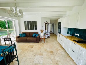 A spacious living area with a brown sofa, a dining table with chairs, and a kitchen with white cabinets and a wooden countertop. - Domaine des Anes - Gîte des Mûriers (Tugéras-Saint-Maurice)