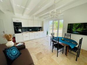 A modern kitchen with white cabinets, a black microwave, and a dining area with a blue tablecloth. - Domaine des Anes - Gîte des Mûriers (Tugéras-Saint-Maurice)