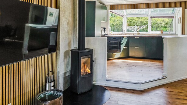 A modern kitchen with a wood-burning stove, a large window, and a built-in TV. - Stunning home in Oksbøl with sauna (Oksbøl)