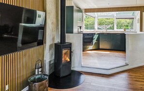 A modern kitchen with a wood-burning stove, a large window, and a built-in TV. - Stunning home in Oksbøl with sauna (Oksbøl)