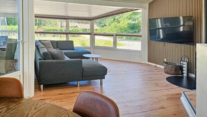 A modern living room with a sectional sofa, a round coffee table, and a flat-screen TV mounted on a wooden wall. - Stunning home in Oksbøl with sauna (Oksbøl)